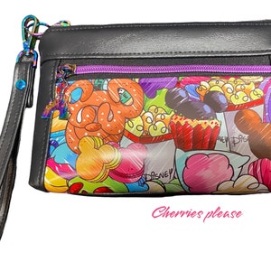 Puede incluir: Una bolsa negra con cremallera con un estampado colorido que presenta a Mickey Mouse, Minnie Mouse y otros personajes de Disney. El estampado incluye imágenes de palomitas de maíz, cupcakes y otras golosinas. La bolsa tiene una correa negra con un acento plateado.