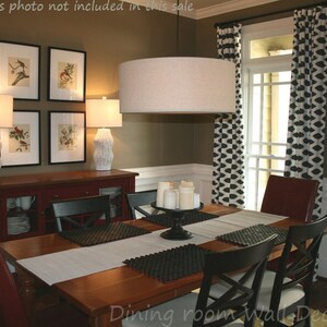 May include: A dining room with a brown wall, a wooden table with black chairs, a red buffet, and a large round light fixture. The windows have black and white patterned curtains. The wall has framed prints of birds.