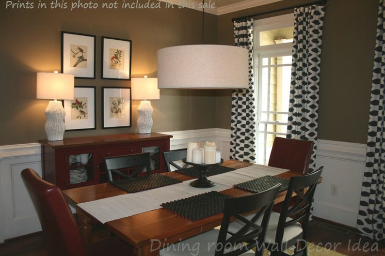 May include: A dining room with a brown wall, a wooden table with black chairs, a red buffet, and a large round light fixture. The windows have black and white patterned curtains. The wall has framed prints of birds.