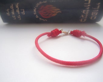May include: A red string bracelet with a silver clasp. The bracelet is tied with a knot at each end.