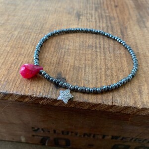 May include: A black beaded bracelet with a pink gemstone and a silver star charm.