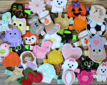 May include: A collection of felt hair clips featuring various designs, including animals, food, and holiday themes. The clips are colorful and whimsical, with a variety of textures and details.