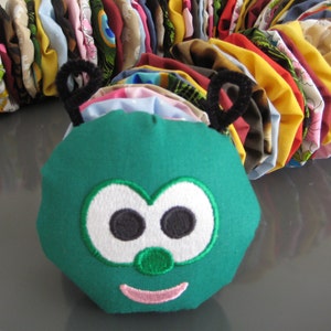 May include: A green fabric caterpillar toy with embroidered eyes, a nose, and a smile. The caterpillar is made up of multiple fabric circles sewn together.