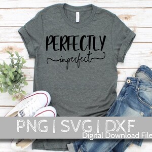 May include: A gray t-shirt with the text "PERFECTLY imperfect" in black lettering. The shirt is displayed on a wooden surface with a pair of white sneakers and blue jeans.