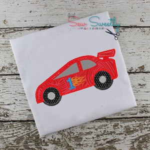May include: Red race car with a number one on the side and flames on the side. The car is on a white t-shirt.