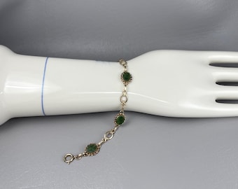 May include: A gold-toned link bracelet featuring three oval-shaped, dark green stone cabochons set in decorative metal frames. The bracelet is constructed with alternating oval metal links and includes a circular spring ring clasp closure.
