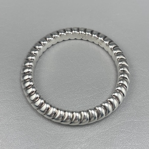 May include: A polished silver ring featuring a continuous, repeating ribbed or twisted texture around the entire band. The metal surface is highly reflective, creating alternating highlights and shadows along the rounded, segmented design of the ring.