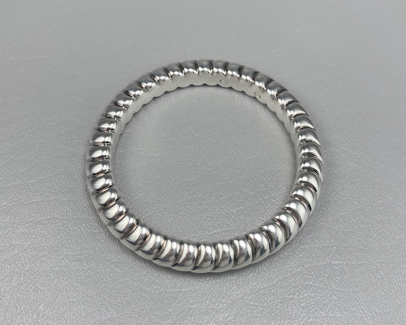 May include: A polished silver ring featuring a continuous, repeating ribbed or twisted texture around the entire band. The metal surface is highly reflective, creating alternating highlights and shadows along the rounded, segmented design of the ring.