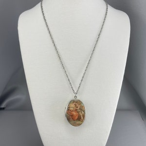May include: A silver chain necklace with an oval locket featuring a vintage-style image of two figures in a romantic embrace.