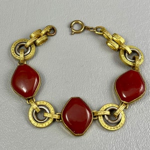 May include: A gold tone bracelet with three red gemstone accents. The bracelet has a decorative chain link design.