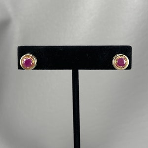 May include: A pair of gold stud earrings with a round, dark pink gemstone in each.