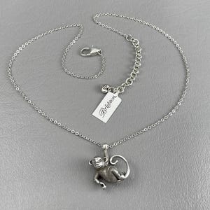 Peut inclure: Collier argent&eacute; avec un pendentif singe d&eacute;taill&eacute;. Le singe est suspendu &agrave; une branche. La cha&icirc;ne est fine et se ferme avec un fermoir mousqueton. Une &eacute;tiquette blanche avec la marque "Brighton" est attach&eacute;e.
