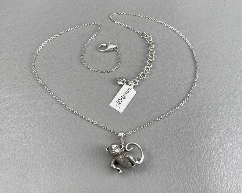 Peut inclure: Collier argent&eacute; avec un pendentif singe d&eacute;taill&eacute;. Le singe est suspendu &agrave; une branche. La cha&icirc;ne est fine et se ferme avec un fermoir mousqueton. Une &eacute;tiquette blanche avec la marque "Brighton" est attach&eacute;e.
