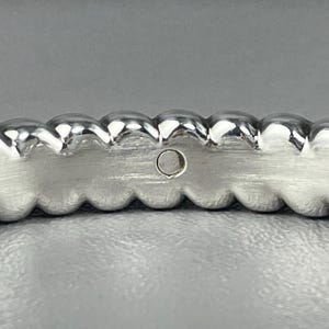 May include: A silver-toned ring featuring a continuous row of rounded, bead-like spheres along the top edge. The inner band has a brushed metal finish and includes a small, circular hallmark stamp containing faint, illegible text.