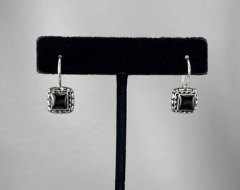 May include: A pair of silver drop earrings featuring square-shaped black stones set in a textured silver frame. Each earring hangs from a curved silver hook, showcasing a polished black center surrounded by a detailed, beaded silver border design.