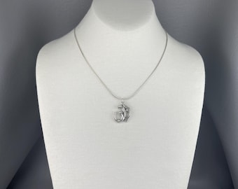 May include: A silver-colored necklace with an Om symbol pendant. The pendant is a stylized representation of the sacred Hindu symbol. The necklace is displayed on a white mannequin.
