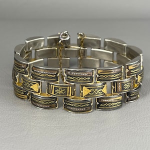 May include: A silver bracelet with a geometric pattern in gold and black enamel. The bracelet is made of linked metal pieces.