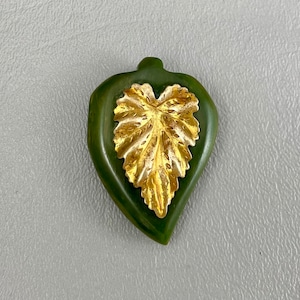May include: A green heart-shaped pendant with a gold leaf design.