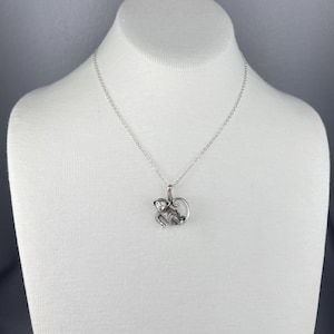 Peut inclure: Un collier avec un pendentif singe argent&eacute;. Le charm en forme de singe, orn&eacute; d'une petite gemme, est suspendu &agrave; une cha&icirc;ne d&eacute;licate. Le collier est pr&eacute;sent&eacute; sur un buste de mannequin blanc sur fond gris.