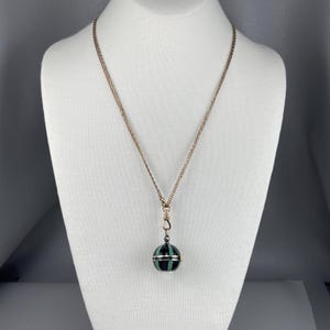 May include: A gold chain necklace with a black and green striped sphere pendant.