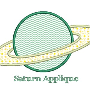May include: Green and yellow applique design of the planet Saturn with a ring of stars. The text "Saturn Applique" is below the design.