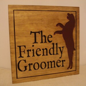 May include: A wooden sign with the text "The Friendly Groomer" and a brown silhouette of a dog standing on its hind legs.