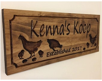 May include: Wooden sign with the text "Kenna's Koop" and "Established 2017". The sign features carved images of chickens, chicks, and eggs. The sign is made of stained wood with a decorative border.