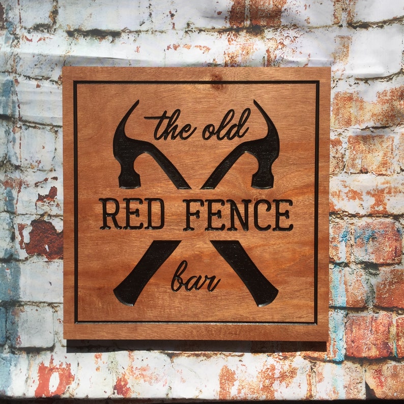 May include: A wooden sign with a brown background and black text. The sign reads "The Old Red Fence Bar" with two crossed hammers.