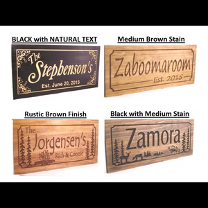 May include: Four wooden signs with different stain colours and engraved text. The signs feature different styles of text and designs, including a deer, trees, and a campfire. The text on the signs reads "The Stepbenson's Est. June 20, 2015", "Zaboomaroom -Est. 2015-", "The Jorgensen's Rich & Connie", and "Zamora".