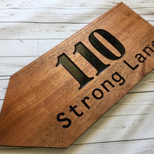 May include: A wooden arrow-shaped sign with the house number 110 and the street name Strong Lane carved into the surface.