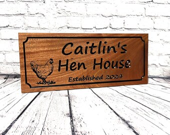 May include: A rectangular wooden sign with a dark border and the words "Caitlin's Hen House" carved into the wood. A detailed illustration of a chicken is on the left. The text "Established 2024" is at the bottom.