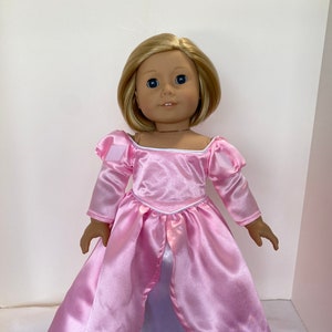 May include: A doll with blonde hair and blue eyes wearing a pink satin dress with long sleeves and a white underskirt. The dress has a square neckline and a fitted bodice.