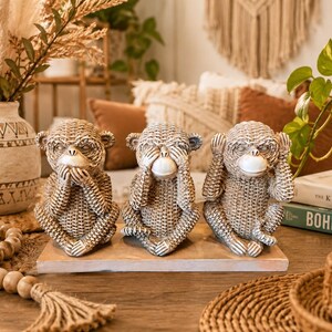 May include: A set of three textured, light brown monkey figurines seated on a rectangular wooden base. The monkeys are depicted in the classic pose of covering their mouth, eyes, and ears with their hands, featuring a woven-like surface finish.