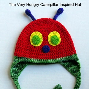 May include: A red, green, and yellow crocheted hat inspired by The Very Hungry Caterpillar book. The hat has a long green braided strap with tassels at each end. "Made By: Maiwear" is written on the white background.