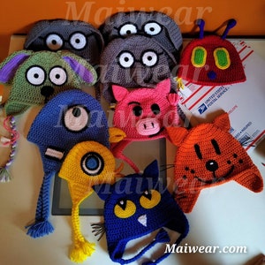 May include: A collection of colorful crocheted hats with different animal faces. The hats feature a variety of characters, including a cat, a pig, a bug, a dog, and a monster. Each hat has a long tail and is made with a soft, textured yarn.