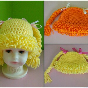 May include: Three crocheted hats with pigtails. The hats are yellow and orange. The pigtails are made of yarn and have pink bows.