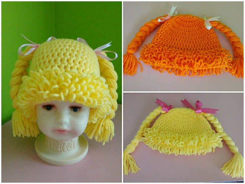 May include: Three crocheted hats with pigtails. The hats are yellow and orange. The pigtails are made of yarn and have pink bows.