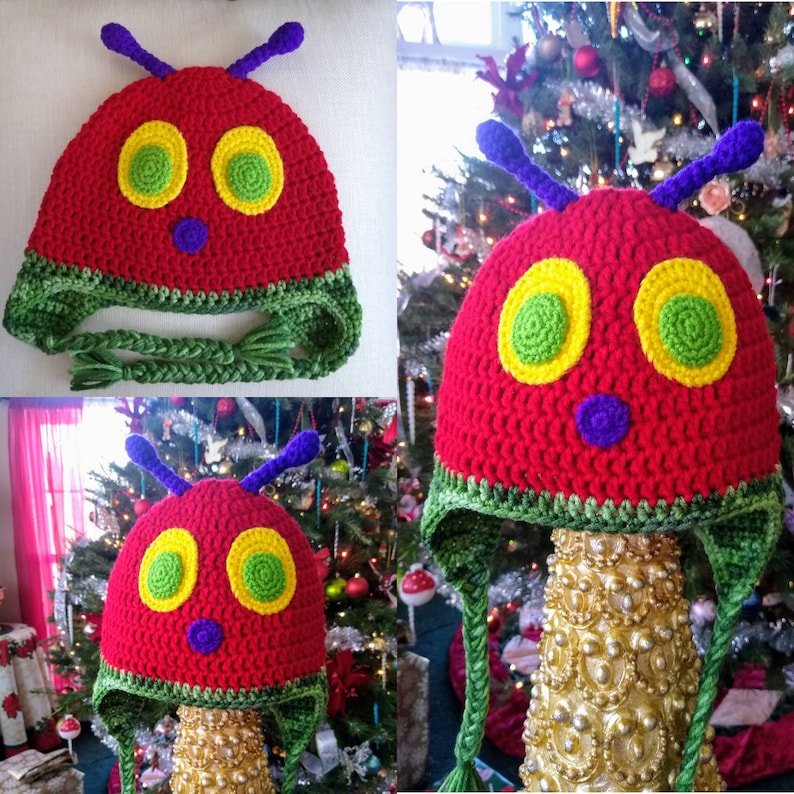 May include: A red and green crocheted hat shaped like the Very Hungry Caterpillar. The hat has large yellow eyes with green pupils, a purple nose, and green antennas.