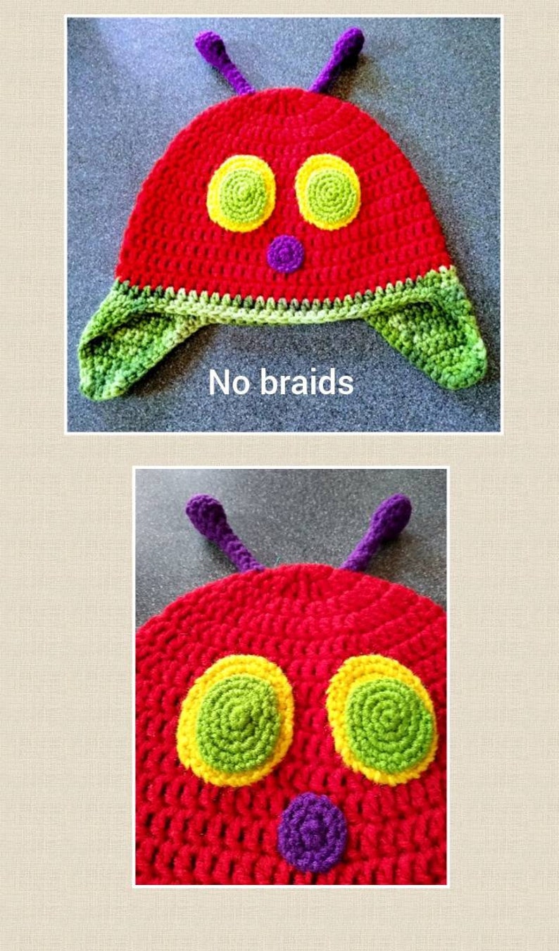 May include: A red crocheted hat with green and yellow eyes, a purple nose, and green ear flaps. The hat is shaped like a caterpillar and has the text "No braids" written below it.