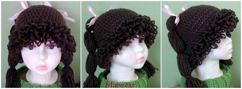 May include: A brown crocheted hat with long brown yarn pigtails and pink bows. The hat is on a mannequin head.