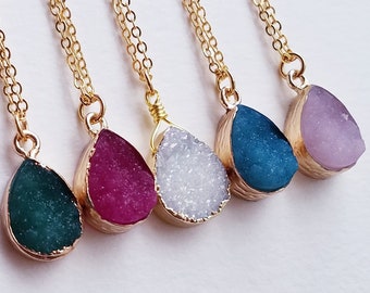 May include: Five gold chain necklaces with teardrop-shaped pendants. The pendants are made of different colored crystals, including green, pink, white, blue, and purple.