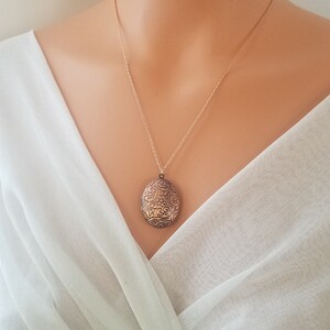 May include: A gold chain necklace with a delicate oval locket pendant featuring an intricate floral design.