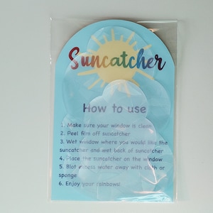 May include: A package of colorful suncatchers with instructions on how to use them. The instructions say to make sure your window is clean, peel the film off the suncatcher, wet the window and the back of the suncatcher, place the suncatcher on the window, blot excess water away with a cloth or sponge, and enjoy your rainbows!
