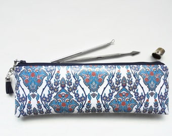 May include: A white zippered pouch with a blue and red floral pattern. The pouch has a tassel on the zipper pull.