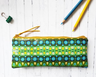 May include: A green and blue floral patterned pencil case with a yellow zipper and a yellow pull tab.