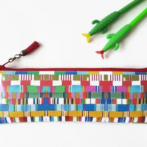 May include: A colorful zippered pencil case with a red tassel. The case has a geometric pattern of red, yellow, blue, green, and white stripes.