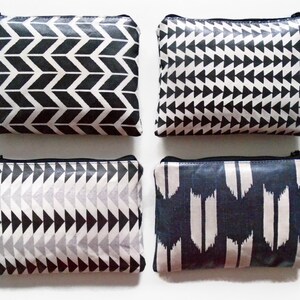 May include: Four rectangular zippered pouches with black and white geometric patterns. Each pouch has a black tassel and a metal zipper. The patterns include chevrons, triangles, and abstract shapes.