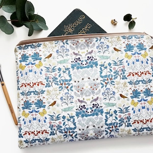 May include: A white zippered pouch with a floral and bird print. The print features blue, green, yellow, red, and brown colors. The pouch has a brown tassel zipper pull.