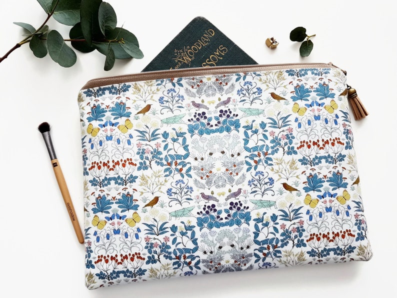 May include: A white zippered pouch with a floral and bird print. The print features blue, green, yellow, red, and brown colors. The pouch has a brown tassel zipper pull.