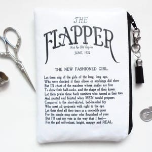 May include: A white zippered pouch with black trim and a tassel zipper pull. The pouch features a black and white print of a poem titled "The Flapper" with the text "Not For Old Fogies June, 1922" and "The New Fashioned Girl."